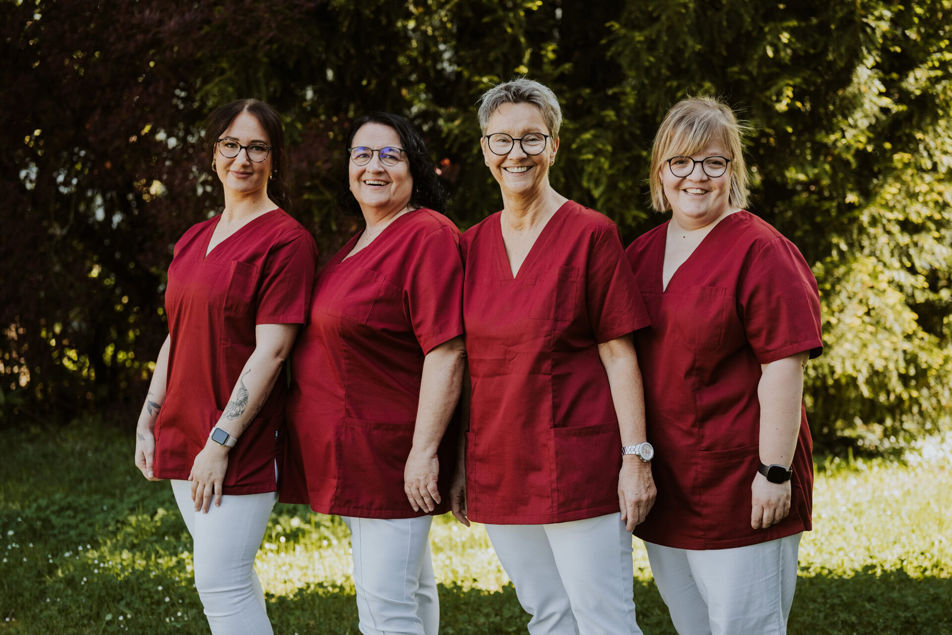 Pflegepersonal in roter Arbeitskleidung bei Sonnenlicht in Grünanlage, Teamarbeit in der Onkologie.